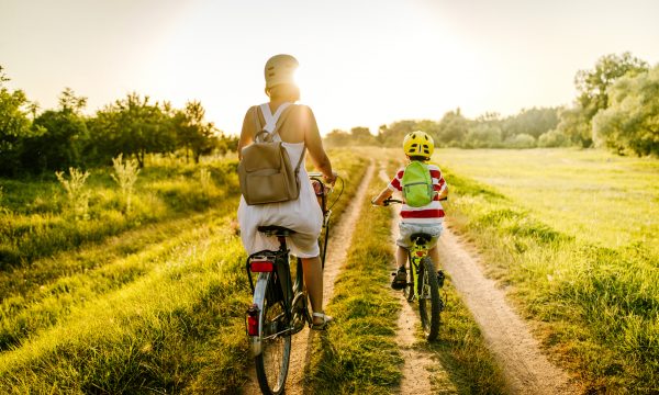 Photo of a young boy riding a bicycle with his mother on a beautiful sunny day in nature